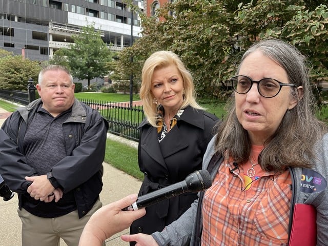 Lea Maceyko, speaking, alongside Tammy Krings and Arthur “Ed” Dunn.