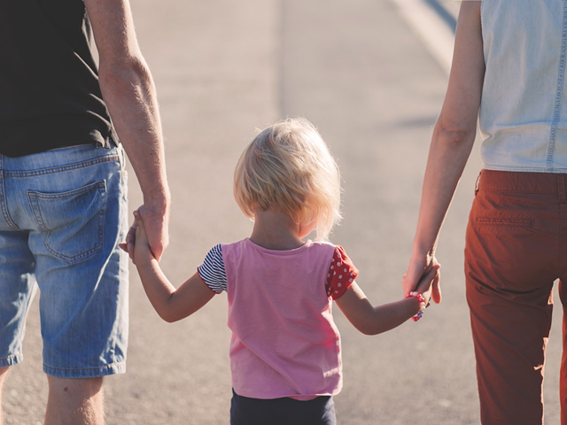 little blonde girl between two adults holds their hands