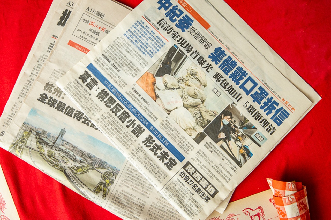 A stack of Chinese newspapers sitting on a chair in the back of the dining room