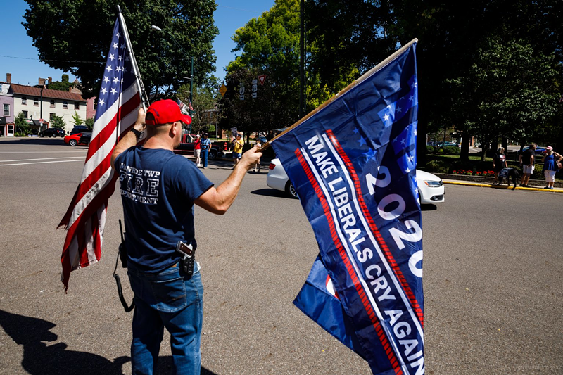 A Trump fan, counter-protesting a “Signs on the Square” event Sept. 5, waves two flags with a holstered pistol at his side. - Photo: Provided by Graham H. Stokes